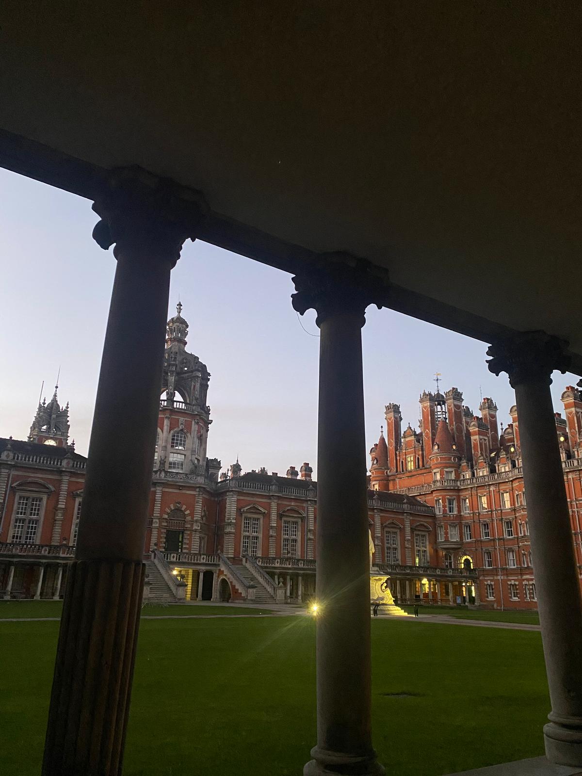 The Royal Holloway quad at dusk, columns and lit windows beyond